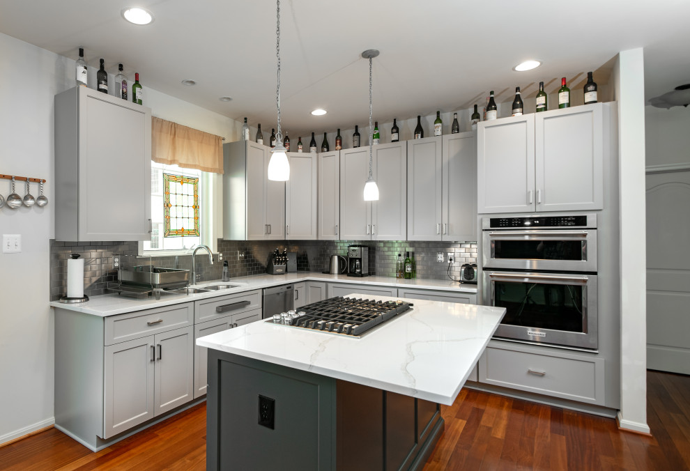 Inredning av ett modernt avskilt, stort vit vitt u-kök, med en undermonterad diskho, skåp i shakerstil, grå skåp, bänkskiva i kvarts, grått stänkskydd, stänkskydd i metallkakel, rostfria vitvaror, mörkt trägolv, en köksö och brunt golv