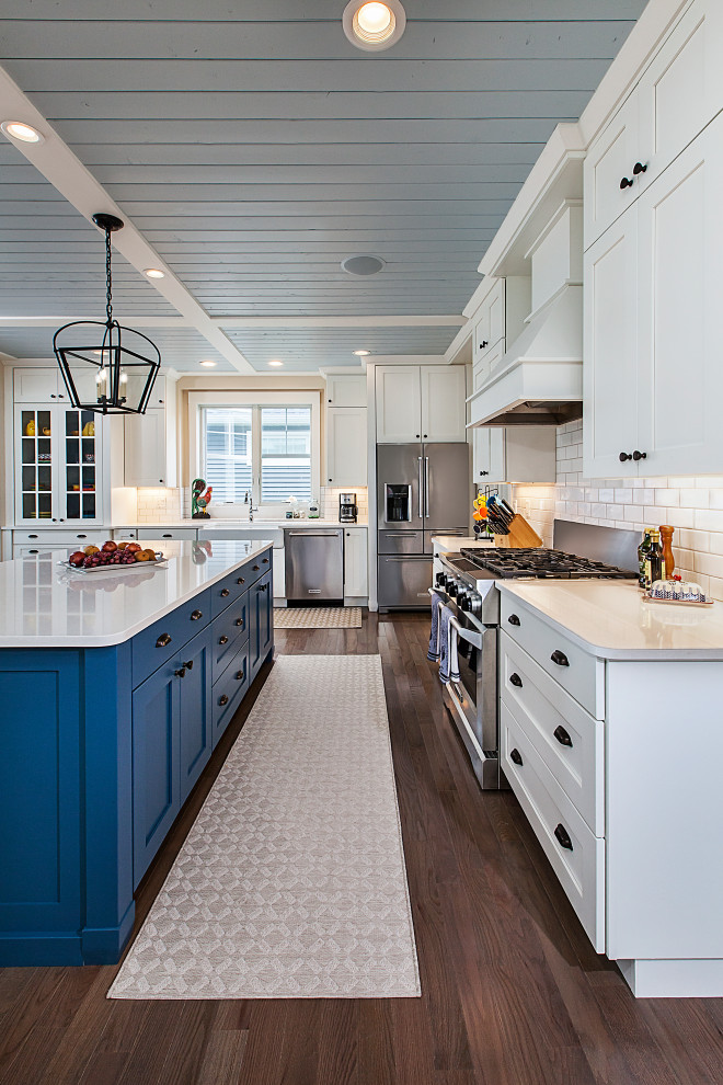 Large beach style l-shaped eat-in kitchen in Grand Rapids with a farmhouse sink, recessed-panel cabinets, white cabinets, quartzite benchtops, white splashback, subway tile splashback, stainless steel appliances, medium hardwood floors, with island and white benchtop.