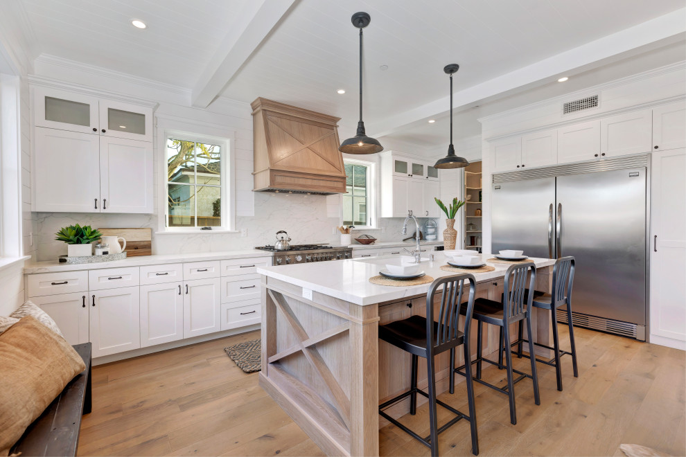 Inspiration for a country u-shaped kitchen in Los Angeles with shaker cabinets, white cabinets, stainless steel appliances, medium hardwood floors, with island, brown floor, white benchtop and timber.