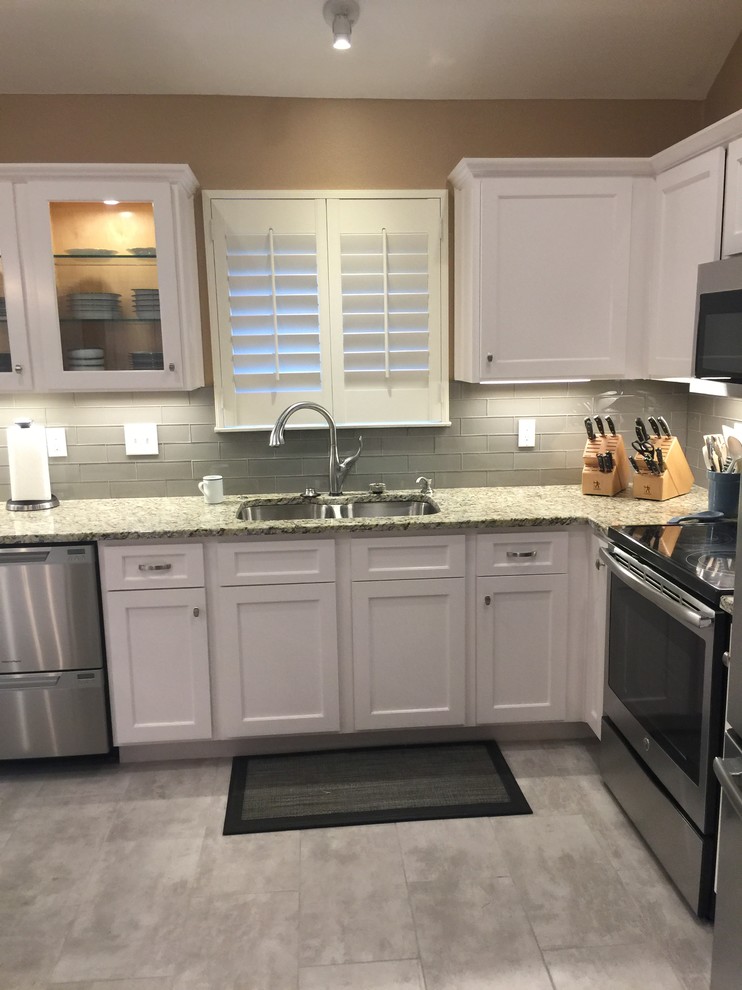 Inspiration for a mid-sized transitional l-shaped porcelain tile eat-in kitchen remodel in Austin with an undermount sink, shaker cabinets, white cabinets, granite countertops, white backsplash, glass tile backsplash, stainless steel appliances and an island