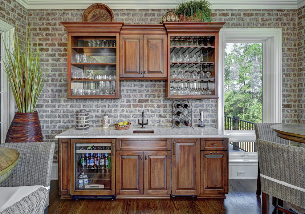 This is an example of a traditional single-wall wet bar in Charleston with an undermount sink, raised-panel cabinets, dark wood cabinets, dark hardwood floors and white benchtop.