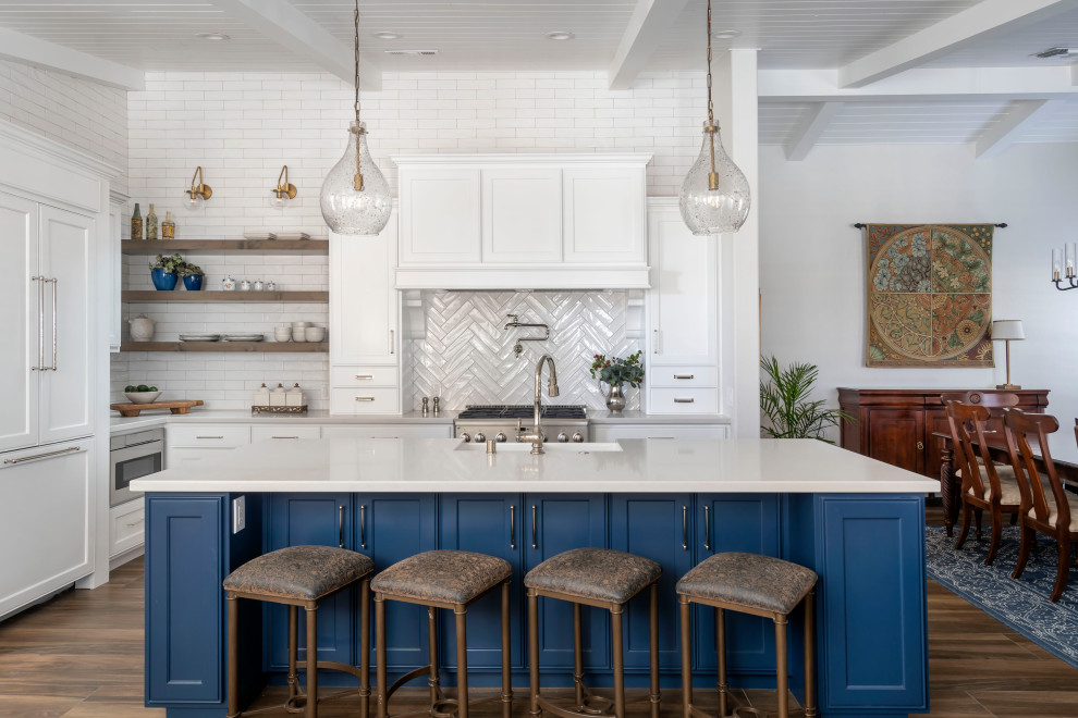 Inspiration for a large traditional l-shaped eat-in kitchen in Los Angeles with a farmhouse sink, recessed-panel cabinets, white cabinets, quartz benchtops, white splashback, ceramic splashback, panelled appliances, ceramic floors, with island, brown floor, white benchtop and wood.