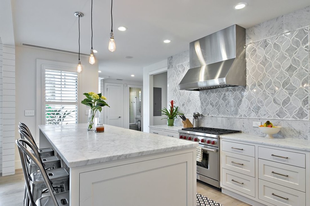 Country kitchen in Austin with a farmhouse sink, shaker cabinets, white cabinets, marble benchtops, grey splashback, stone tile splashback and stainless steel appliances.