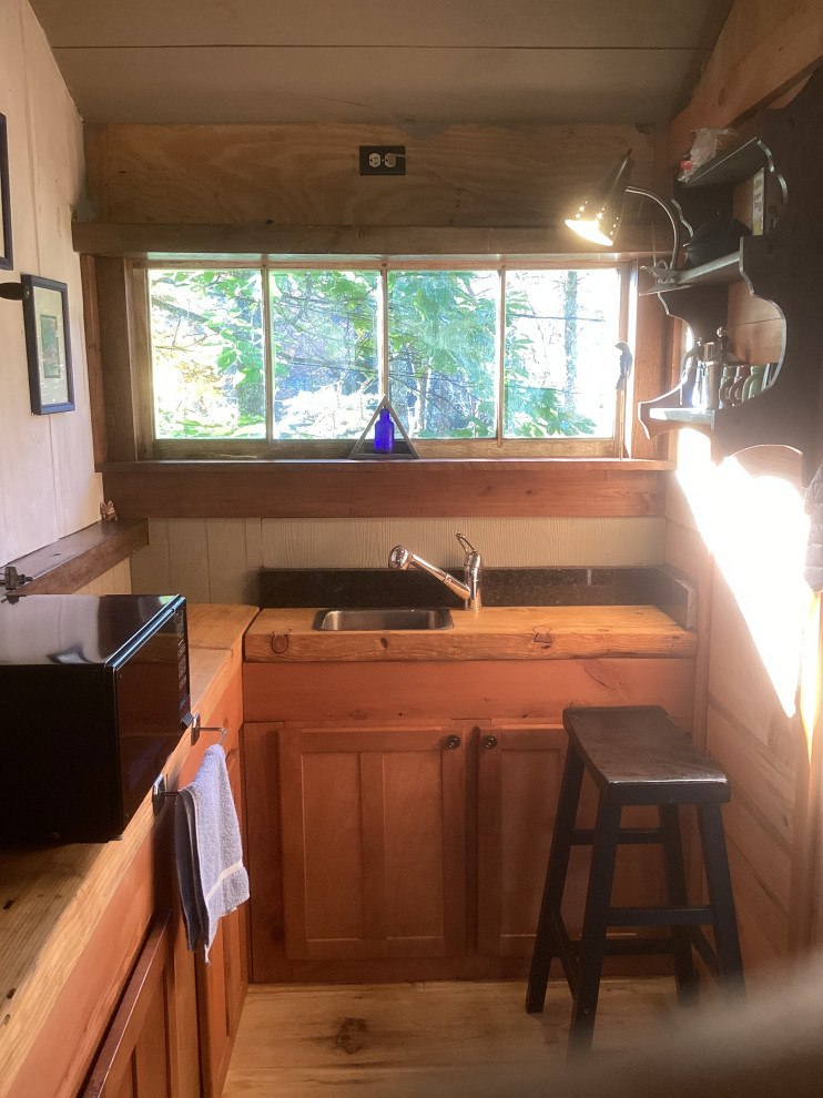 Inspiration for a small rustic l-shaped light wood floor, brown floor and exposed beam eat-in kitchen remodel with a drop-in sink, flat-panel cabinets, light wood cabinets, wood countertops, black backsplash, granite backsplash, stainless steel appliances, no island and brown countertops