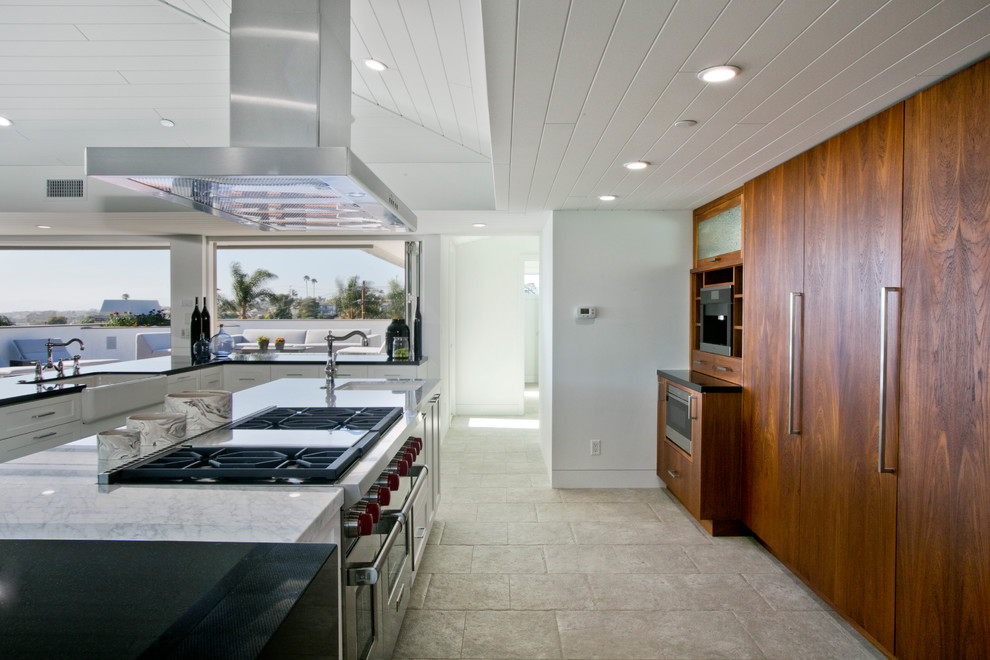 Large contemporary u-shaped open plan kitchen in Los Angeles with a farmhouse sink, flat-panel cabinets, medium wood cabinets, quartzite benchtops, stainless steel appliances, limestone floors and multiple islands.