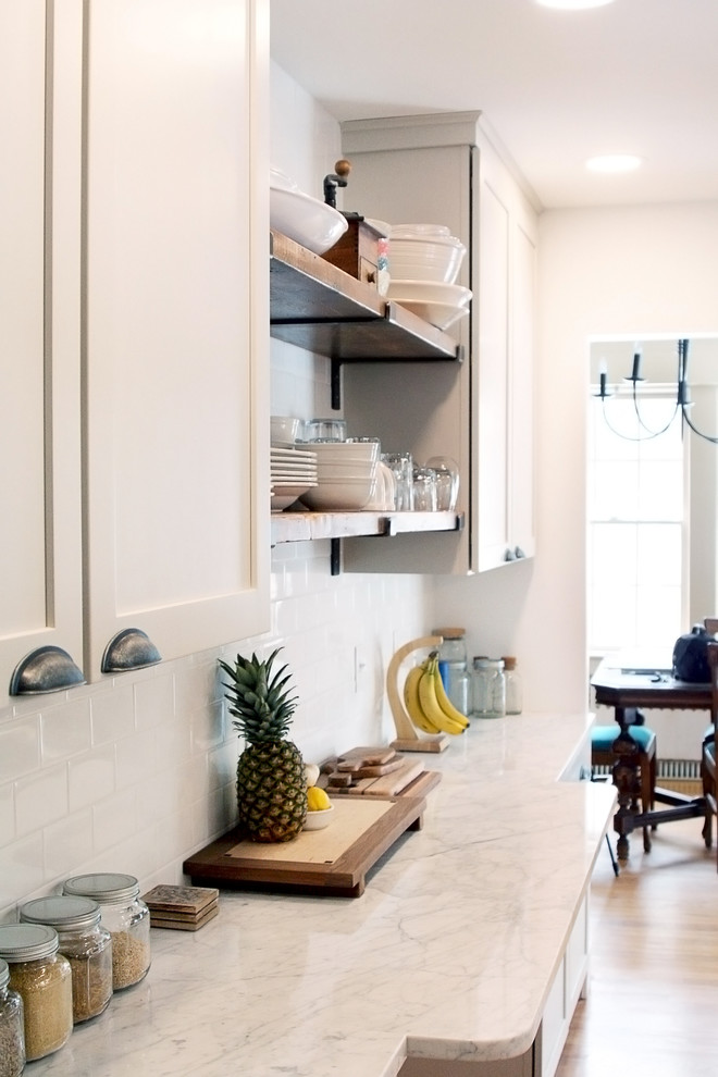 Mid-sized transitional galley medium tone wood floor kitchen pantry photo in Boston with a farmhouse sink, recessed-panel cabinets, white cabinets, marble countertops, white backsplash, subway tile backsplash, stainless steel appliances, an island and white countertops