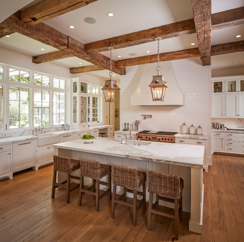 Design ideas for a large traditional u-shaped separate kitchen in Houston with a farmhouse sink, shaker cabinets, white cabinets, white splashback, subway tile splashback, stainless steel appliances, quartzite benchtops, medium hardwood floors, with island and brown floor.