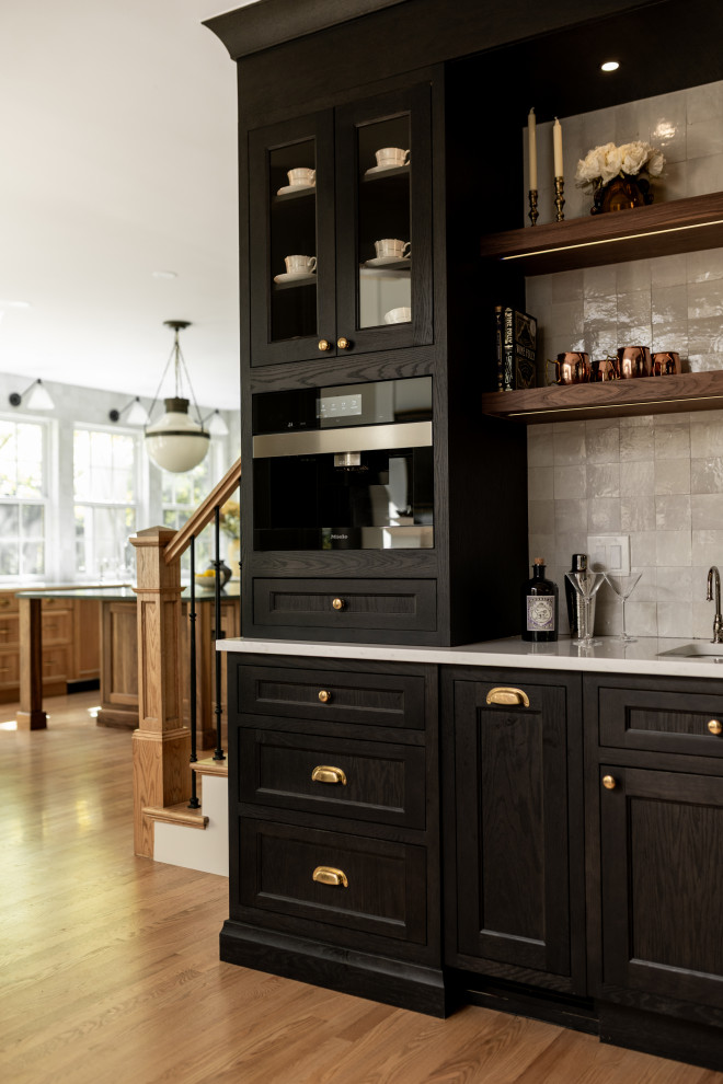 Mid-sized transitional l-shaped light wood floor and brown floor wet bar photo in Detroit with shaker cabinets, white backsplash, black appliances, an island, an undermount sink, black cabinets, quartz countertops, stone tile backsplash and white countertops
