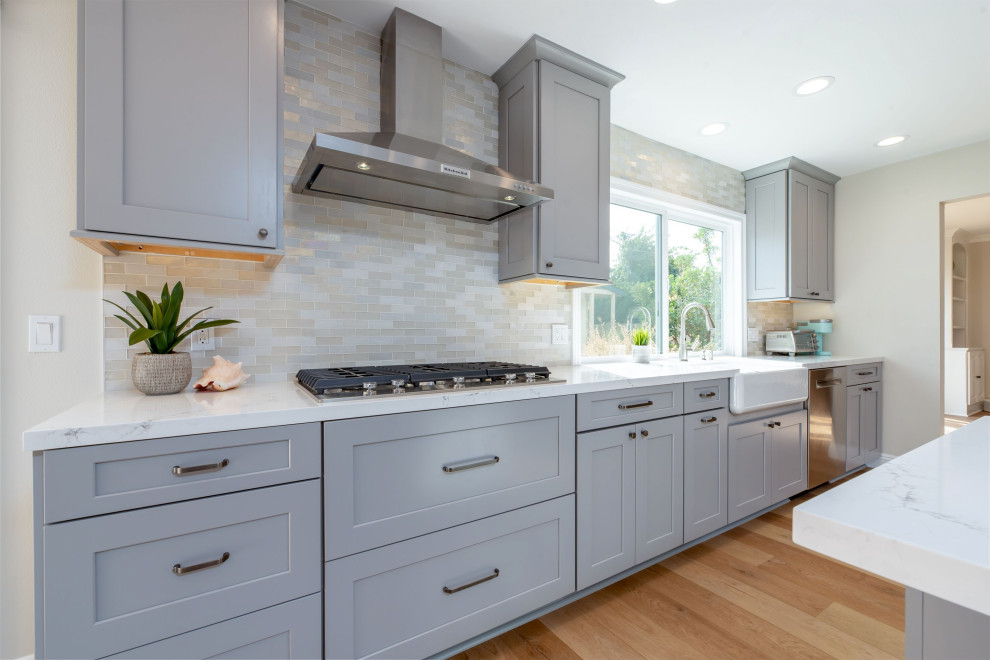Design ideas for a mid-sized transitional kitchen in Orange County with a farmhouse sink, shaker cabinets, grey cabinets, quartz benchtops, white splashback, mosaic tile splashback, stainless steel appliances, laminate floors, with island and white benchtop.