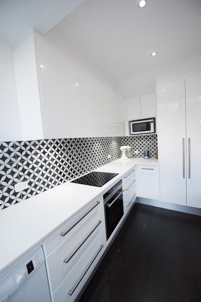 Mid-sized contemporary l-shaped eat-in kitchen in Sydney with flat-panel cabinets, white cabinets, quartz benchtops, black splashback, with island, an undermount sink, porcelain splashback, stainless steel appliances, dark hardwood floors, black floor and white benchtop.