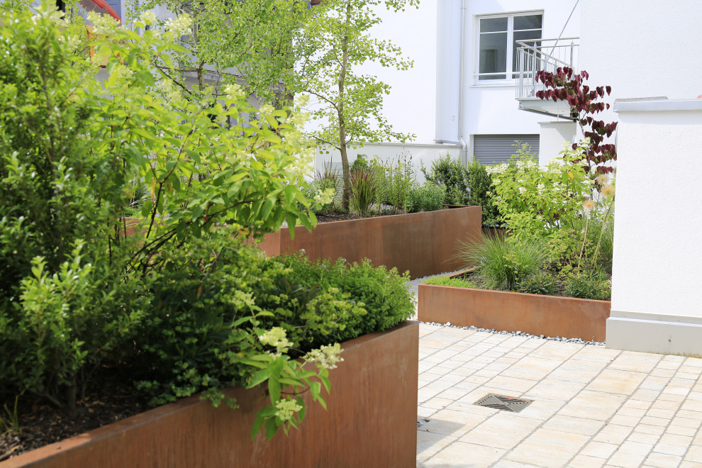 Large contemporary rooftop full sun garden in Munich with with flowerbed and natural stone pavers.
