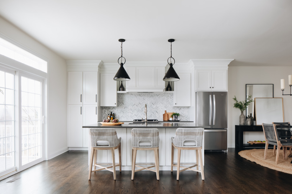 Example of a transitional galley dark wood floor and brown floor kitchen design in Chicago with an undermount sink, shaker cabinets, white cabinets, white backsplash, mosaic tile backsplash, stainless steel appliances, an island and gray countertops
