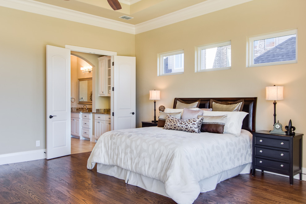 This is an example of an expansive traditional master bedroom in Dallas with yellow walls, dark hardwood floors, no fireplace and brown floor.