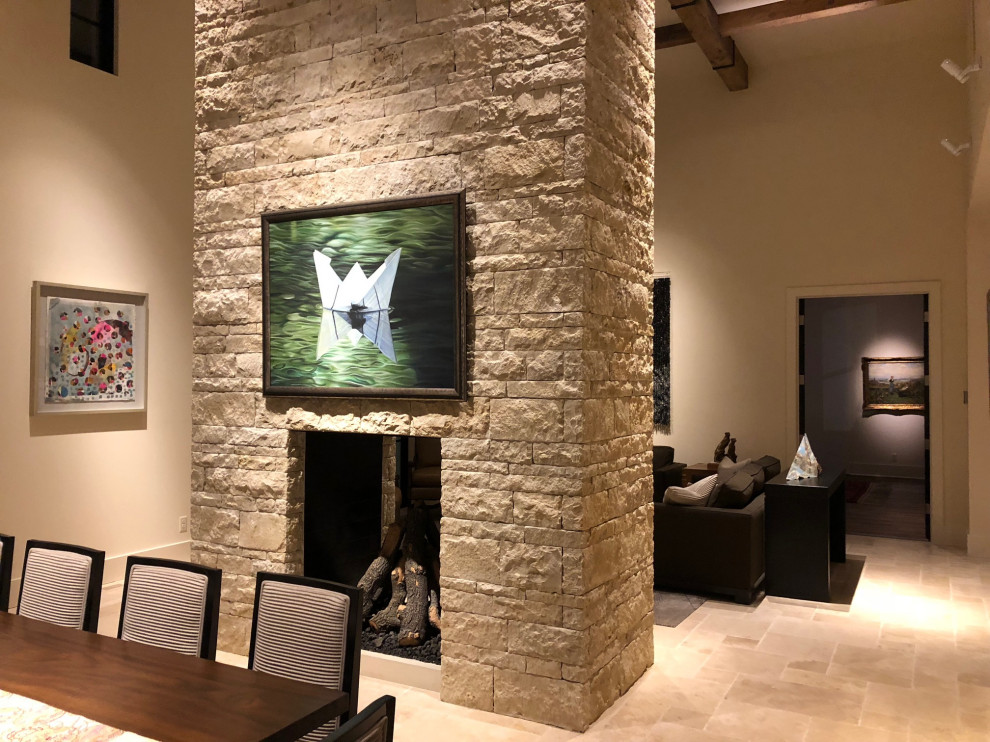 Photo of a mid-sized modern open plan dining in Other with white walls, slate floors, a two-sided fireplace, a stone fireplace surround, beige floor and exposed beam.