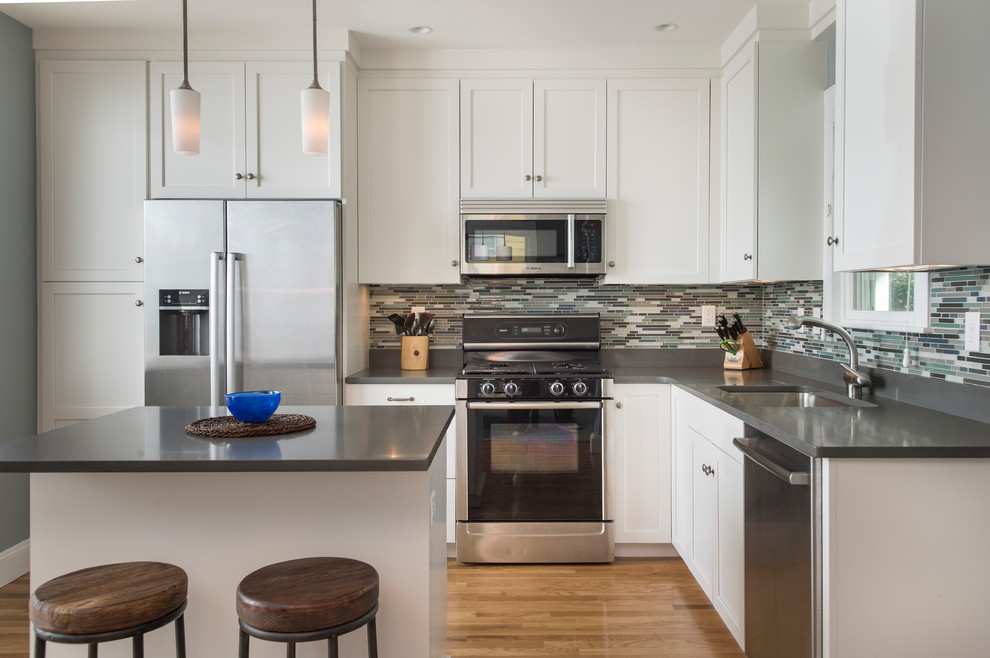 Inspiration for a mid-sized transitional l-shaped medium tone wood floor eat-in kitchen remodel in Boston with an island, shaker cabinets, white cabinets, quartz countertops, gray backsplash, glass sheet backsplash, stainless steel appliances and a single-bowl sink