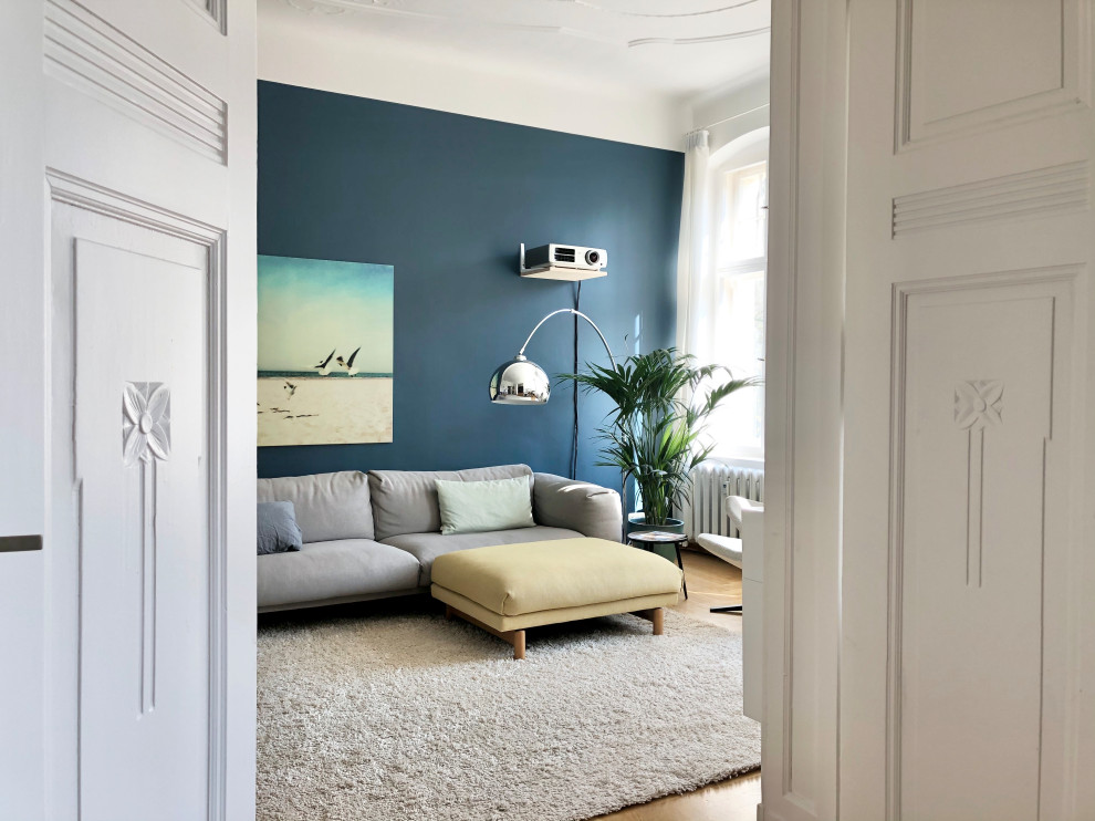This is an example of a large contemporary open concept family room in Berlin with a home bar, blue walls, medium hardwood floors, a wall-mounted tv and brown floor.