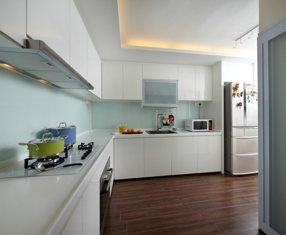 Mid-sized asian l-shaped separate kitchen in Singapore with a single-bowl sink, flat-panel cabinets, white cabinets, solid surface benchtops, white splashback, glass sheet splashback, coloured appliances, porcelain floors and no island.
