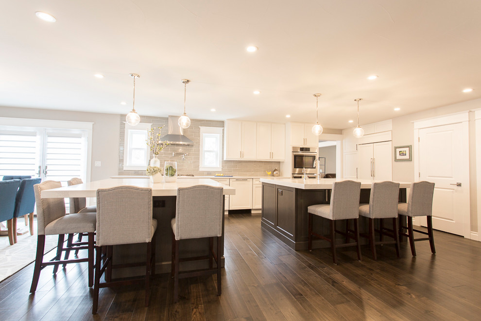 Example of a large transitional l-shaped medium tone wood floor and brown floor eat-in kitchen design in Denver with a single-bowl sink, recessed-panel cabinets, white cabinets, quartz countertops, gray backsplash, ceramic backsplash, stainless steel appliances and two islands