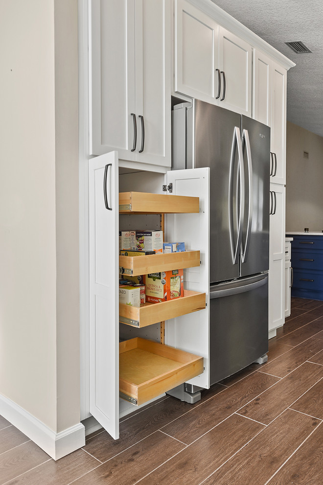 Open concept kitchen - large transitional l-shaped vinyl floor and brown floor open concept kitchen idea in Jacksonville with an undermount sink, shaker cabinets, blue cabinets, quartzite countertops, white backsplash, ceramic backsplash, stainless steel appliances and a peninsula