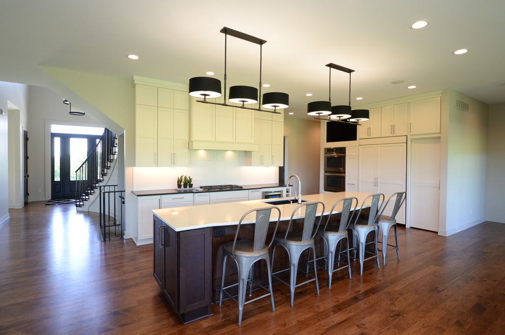 Open concept kitchen - large transitional single-wall medium tone wood floor open concept kitchen idea with an undermount sink, recessed-panel cabinets, white cabinets, granite countertops, white backsplash, stainless steel appliances and an island