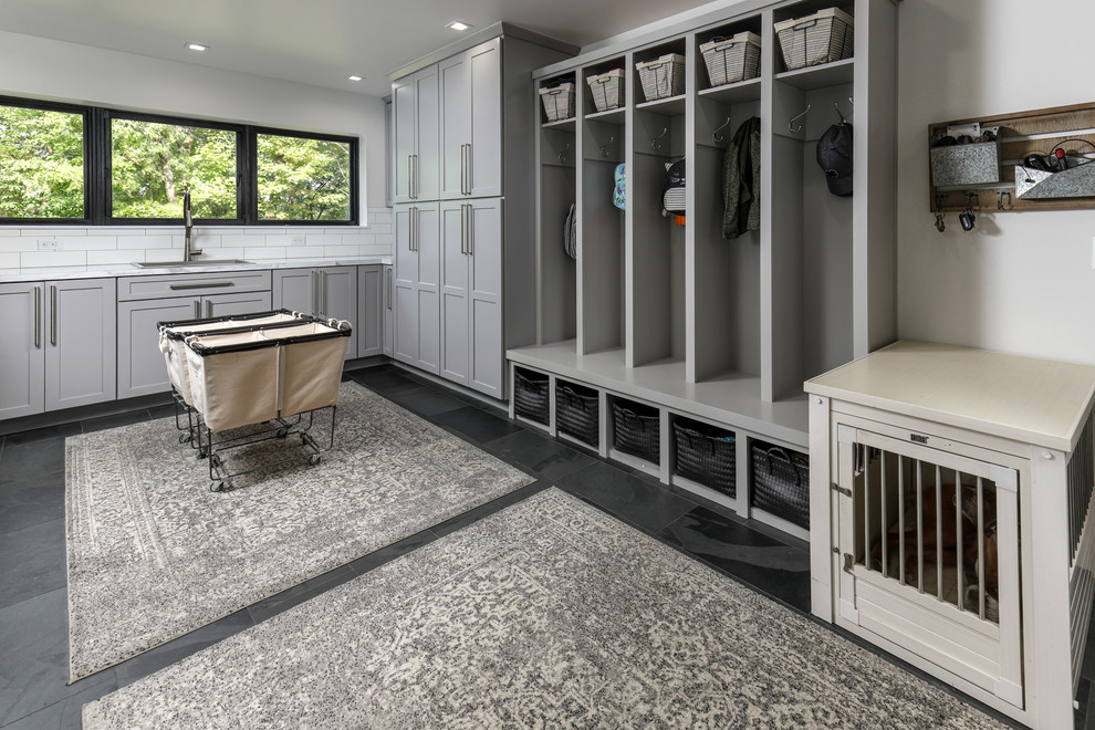 Photo of a mid-sized country l-shaped utility room in Other with a drop-in sink, grey cabinets, white walls, porcelain floors, grey floor, white benchtop and shaker cabinets.