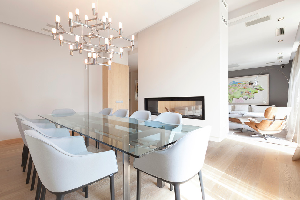 Design ideas for a mid-sized modern open plan dining in Madrid with white walls, light hardwood floors, a plaster fireplace surround and a two-sided fireplace.