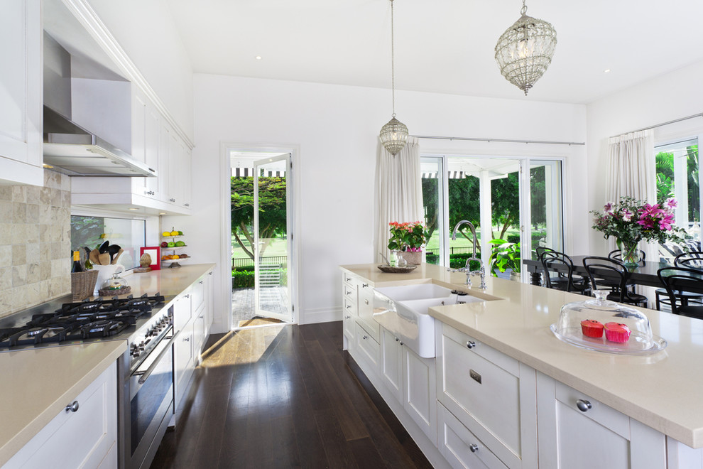 Inspiration for a mid-sized beach style galley open plan kitchen in Los Angeles with a double-bowl sink, flat-panel cabinets, white cabinets, marble benchtops, beige splashback, ceramic splashback, stainless steel appliances, dark hardwood floors and with island.