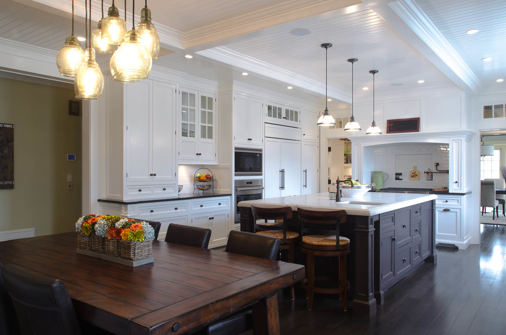 This is an example of a large traditional u-shaped eat-in kitchen in New York with a double-bowl sink, recessed-panel cabinets, white cabinets, marble benchtops, white splashback, glass tile splashback, stainless steel appliances, dark hardwood floors and with island.
