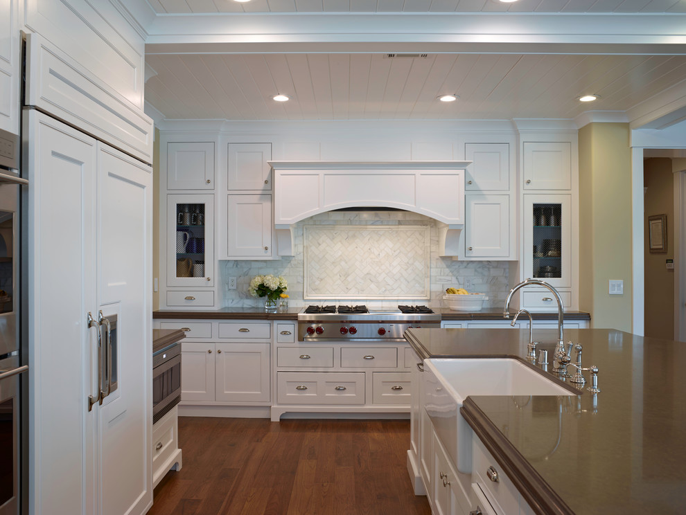 Inspiration for a mid-sized transitional l-shaped medium tone wood floor eat-in kitchen remodel with a farmhouse sink, recessed-panel cabinets, white cabinets, solid surface countertops, white backsplash, stone tile backsplash, stainless steel appliances and an island