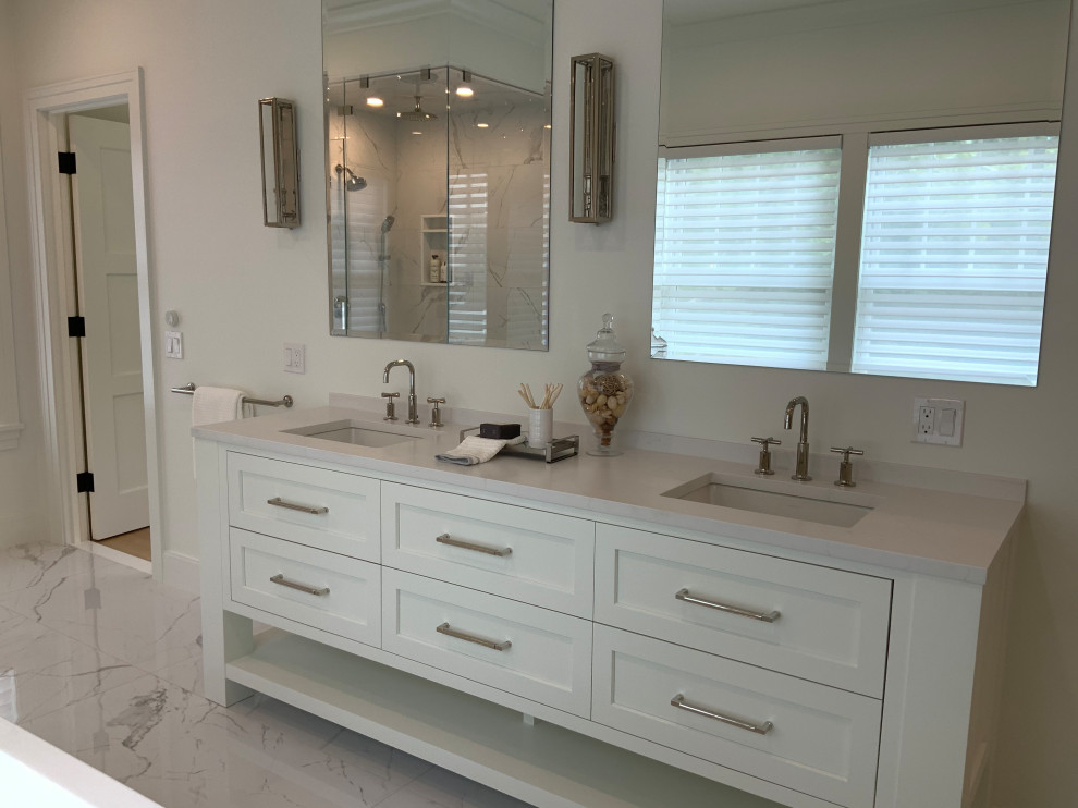 Photo of a large classic ensuite bathroom in Boston with recessed-panel cabinets, white cabinets, a freestanding bath, a corner shower, a two-piece toilet, white tiles, marble tiles, white walls, marble flooring, a submerged sink, engineered stone worktops, white floors, a hinged door, white worktops, an enclosed toilet, double sinks and a built in vanity unit.