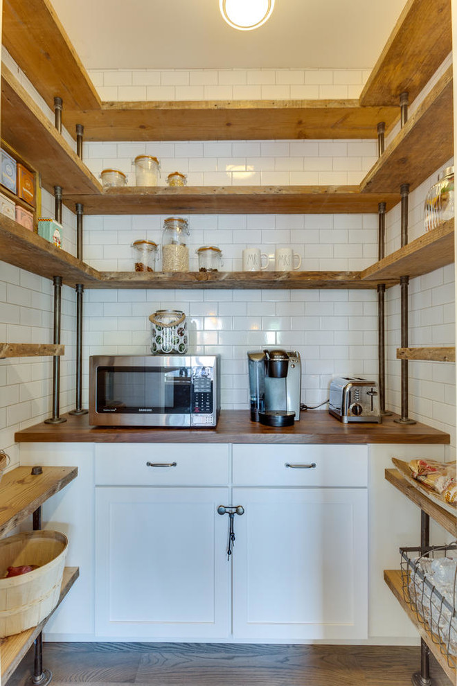 This is an example of a mid-sized country u-shaped kitchen pantry in DC Metro with white cabinets, wood benchtops, white splashback, stainless steel appliances, medium hardwood floors, subway tile splashback, an undermount sink, shaker cabinets and with island.