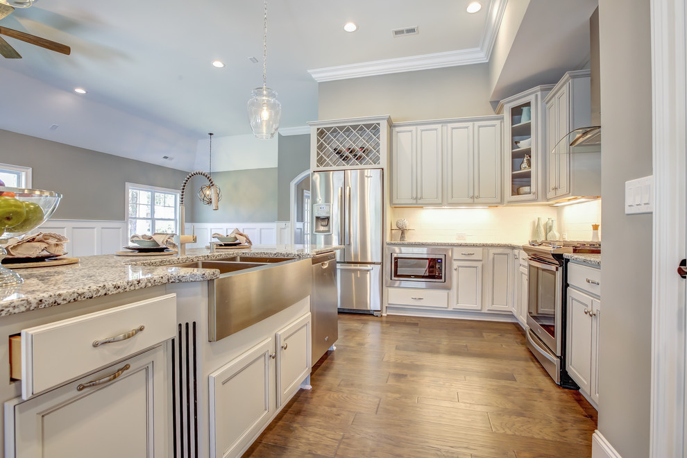 Eat-in kitchen - mid-sized transitional l-shaped medium tone wood floor and brown floor eat-in kitchen idea with a farmhouse sink, recessed-panel cabinets, white cabinets, granite countertops, white backsplash, glass tile backsplash, stainless steel appliances and an island