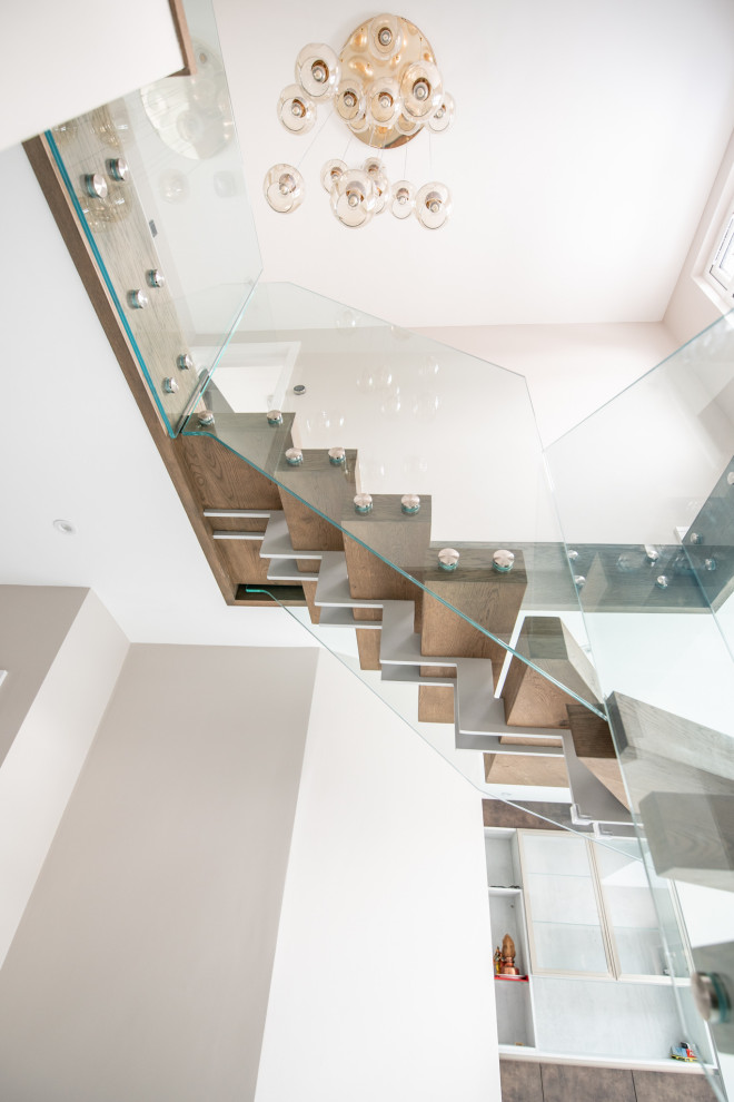 Inspiration for a mid-sized contemporary wood l-shaped staircase in London with open risers and glass railing.