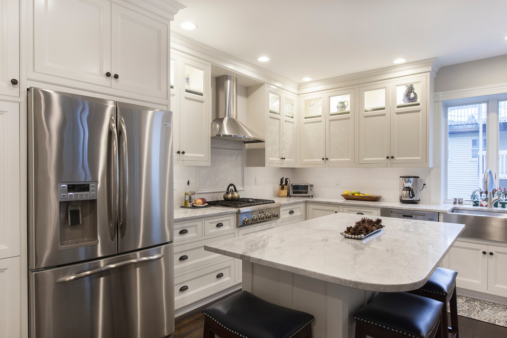 Design ideas for a mid-sized transitional l-shaped kitchen in Boston with a farmhouse sink, shaker cabinets, white cabinets, marble benchtops, white splashback, subway tile splashback, stainless steel appliances, dark hardwood floors and with island.