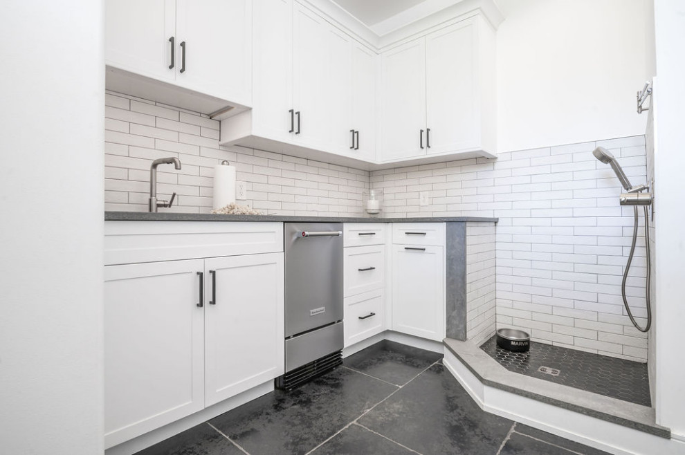 This is an example of a modern utility room in Baltimore with an undermount sink, shaker cabinets, white cabinets, beige splashback, matchstick tile splashback, white walls, black floor and grey benchtop.