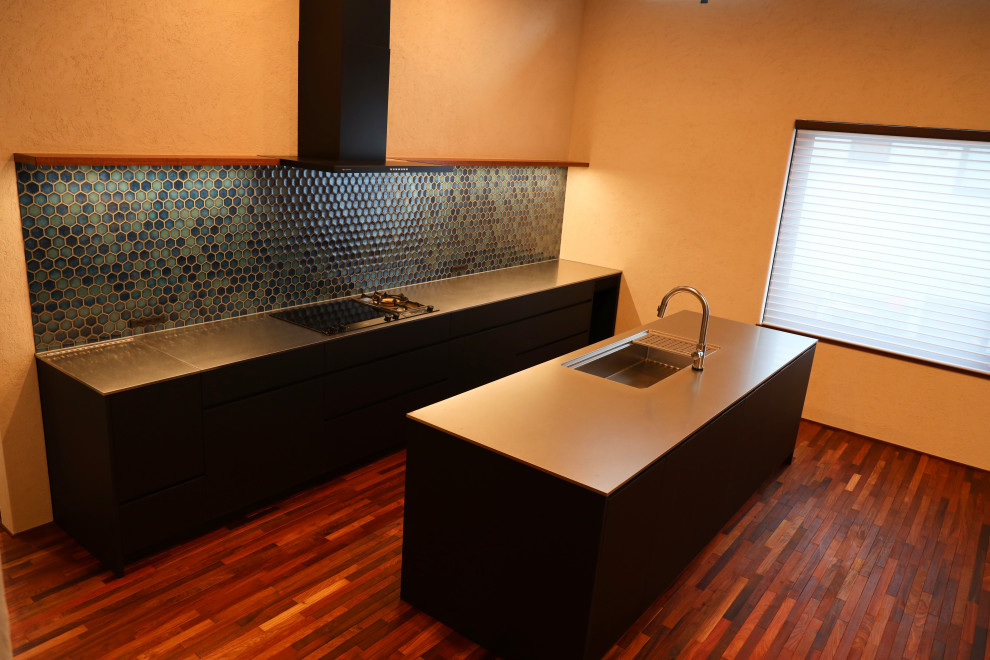 Küche mit schwarzen Schränken, Küchenrückwand in Blau, dunklem Holzboden, Kücheninsel, braunem Boden, grauer Arbeitsplatte und freigelegten Dachbalken in Sapporo
