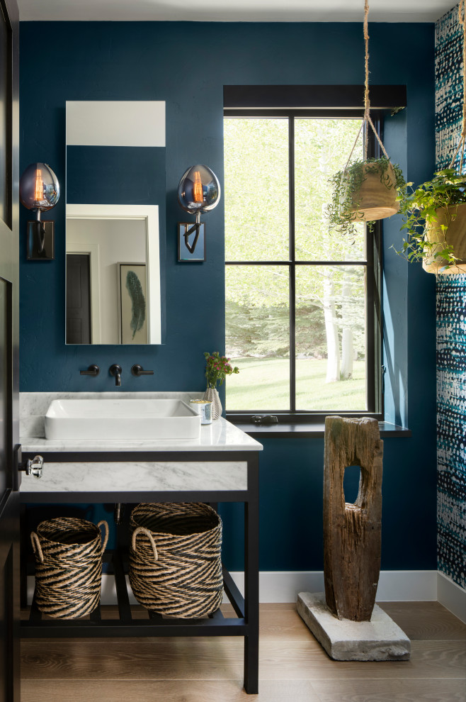 Photo of a country powder room in Denver with blue walls, medium hardwood floors, a vessel sink, brown floor, white benchtops and wallpaper.