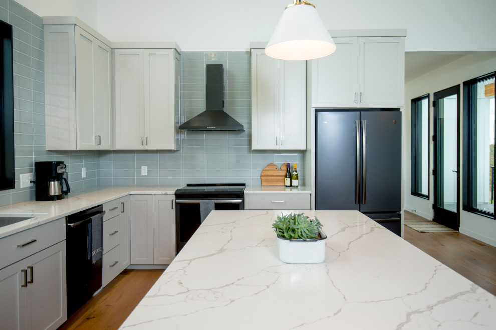 Mid-sized transitional l-shaped kitchen in Other with an undermount sink, shaker cabinets, grey cabinets, green splashback, subway tile splashback, black appliances, with island, white benchtop, light hardwood floors and beige floor.