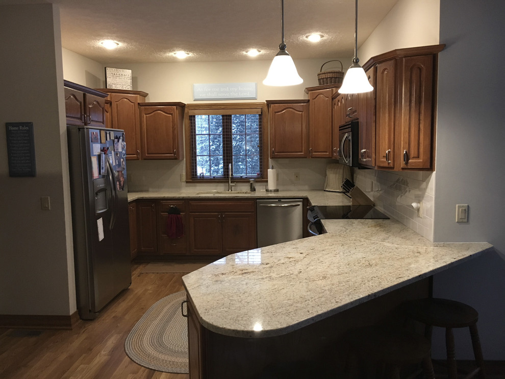 Eat-in kitchen - large transitional u-shaped medium tone wood floor eat-in kitchen idea with an undermount sink, raised-panel cabinets, medium tone wood cabinets, granite countertops, white backsplash, ceramic backsplash, stainless steel appliances and an island