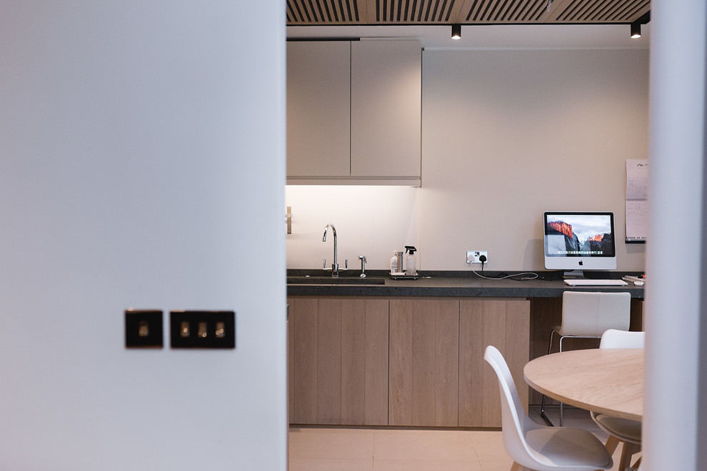 Photo of a mid-sized contemporary u-shaped open plan kitchen in London with flat-panel cabinets, medium wood cabinets, limestone benchtops, white splashback, porcelain splashback, porcelain floors, with island, beige floor, green benchtop, a drop-in sink and stainless steel appliances.