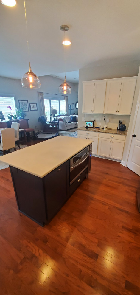 This is an example of a medium sized classic u-shaped kitchen/diner in Raleigh with a double-bowl sink, shaker cabinets, white cabinets, engineered stone countertops, white splashback, ceramic splashback, stainless steel appliances, medium hardwood flooring, an island, brown floors and white worktops.