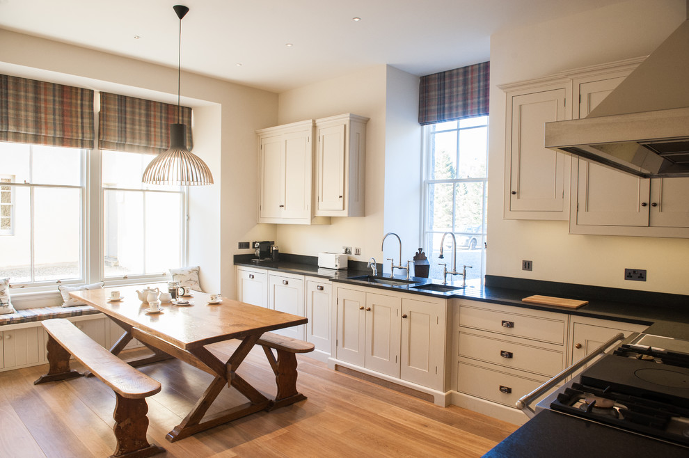 This is an example of a country l-shaped eat-in kitchen in Wiltshire with an undermount sink, recessed-panel cabinets, white cabinets, light hardwood floors and no island.
