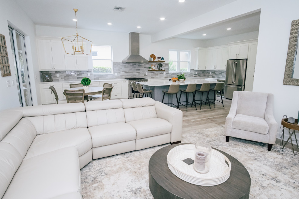 Large traditional l-shaped open plan kitchen in Tampa with a submerged sink, shaker cabinets, white cabinets, engineered stone countertops, grey splashback, ceramic splashback, stainless steel appliances, vinyl flooring, an island, brown floors and white worktops.