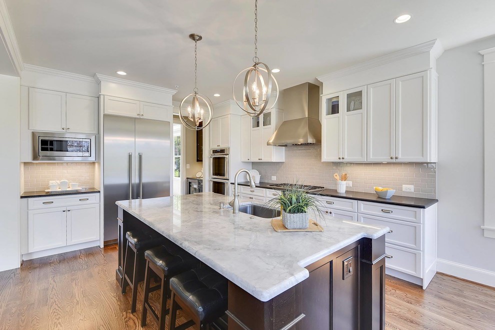 Photo of a mid-sized traditional l-shaped open plan kitchen in DC Metro with an undermount sink, recessed-panel cabinets, quartzite benchtops, grey splashback, subway tile splashback, stainless steel appliances, medium hardwood floors, with island, white benchtop, white cabinets and brown floor.