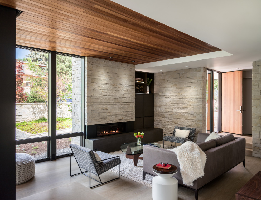 Photo of a mid-sized contemporary open concept living room in Denver with light hardwood floors, a standard fireplace, a stone fireplace surround, a concealed tv and wood.