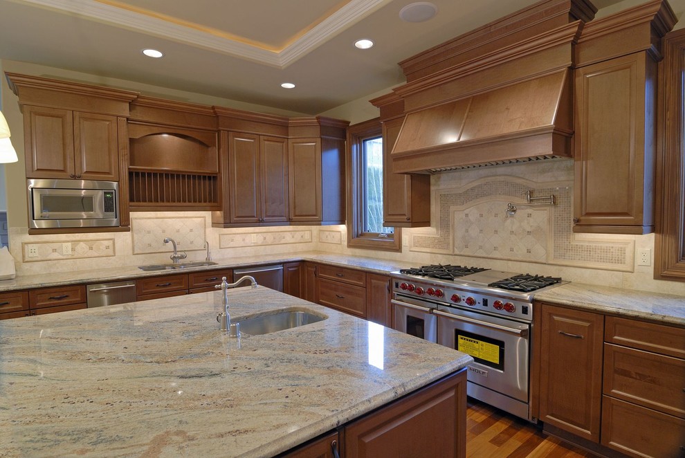 Photo of a large traditional l-shaped eat-in kitchen in Miami with an undermount sink, raised-panel cabinets, light wood cabinets, granite benchtops, white splashback, stone tile splashback, stainless steel appliances, bamboo floors and with island.