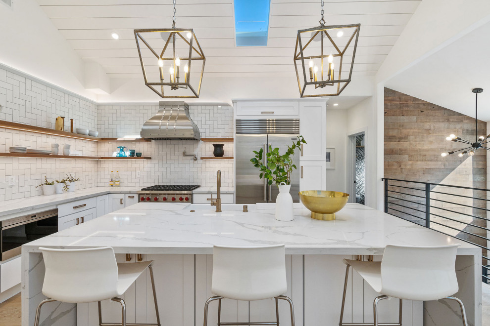 Photo of a large transitional l-shaped kitchen in San Francisco with a farmhouse sink, shaker cabinets, white cabinets, white splashback, subway tile splashback, stainless steel appliances, with island, beige floor and white benchtop.