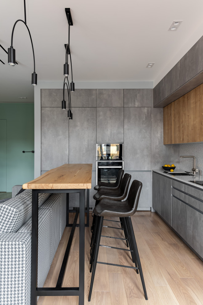Foto på ett mellanstort funkis grå kök, med en enkel diskho, släta luckor, grå skåp, bänkskiva i koppar, grått stänkskydd, svarta vitvaror, mellanmörkt trägolv, en köksö och brunt golv