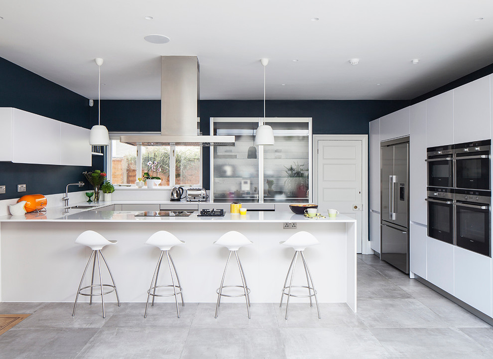 Large contemporary open plan kitchen in Sussex with a drop-in sink, flat-panel cabinets, white cabinets, laminate benchtops, white splashback, stainless steel appliances, concrete floors and with island.