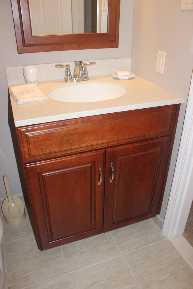 This is an example of a small traditional bathroom in Philadelphia with raised-panel cabinets, medium wood cabinets, an alcove tub, an alcove shower, a two-piece toilet, beige tile, porcelain tile, grey walls, porcelain floors, an integrated sink and solid surface benchtops.